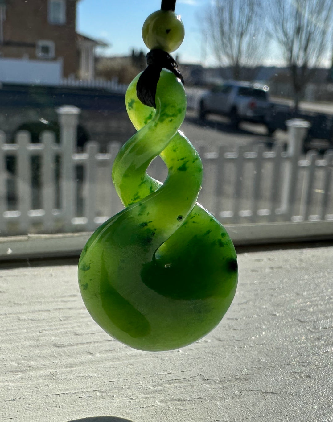 Bright lime green spiral pendant hanging from a black cord with a sunny outdoor background