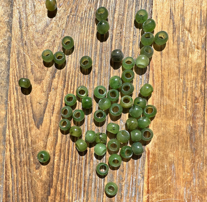 Cluster of 6mm Canadian Jade beads with large holes scattered on a wooden surface