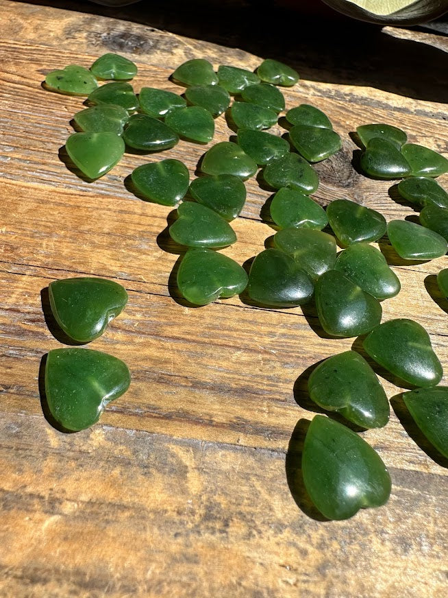 Green jade heart beads on a wooden surface showing drilled holes