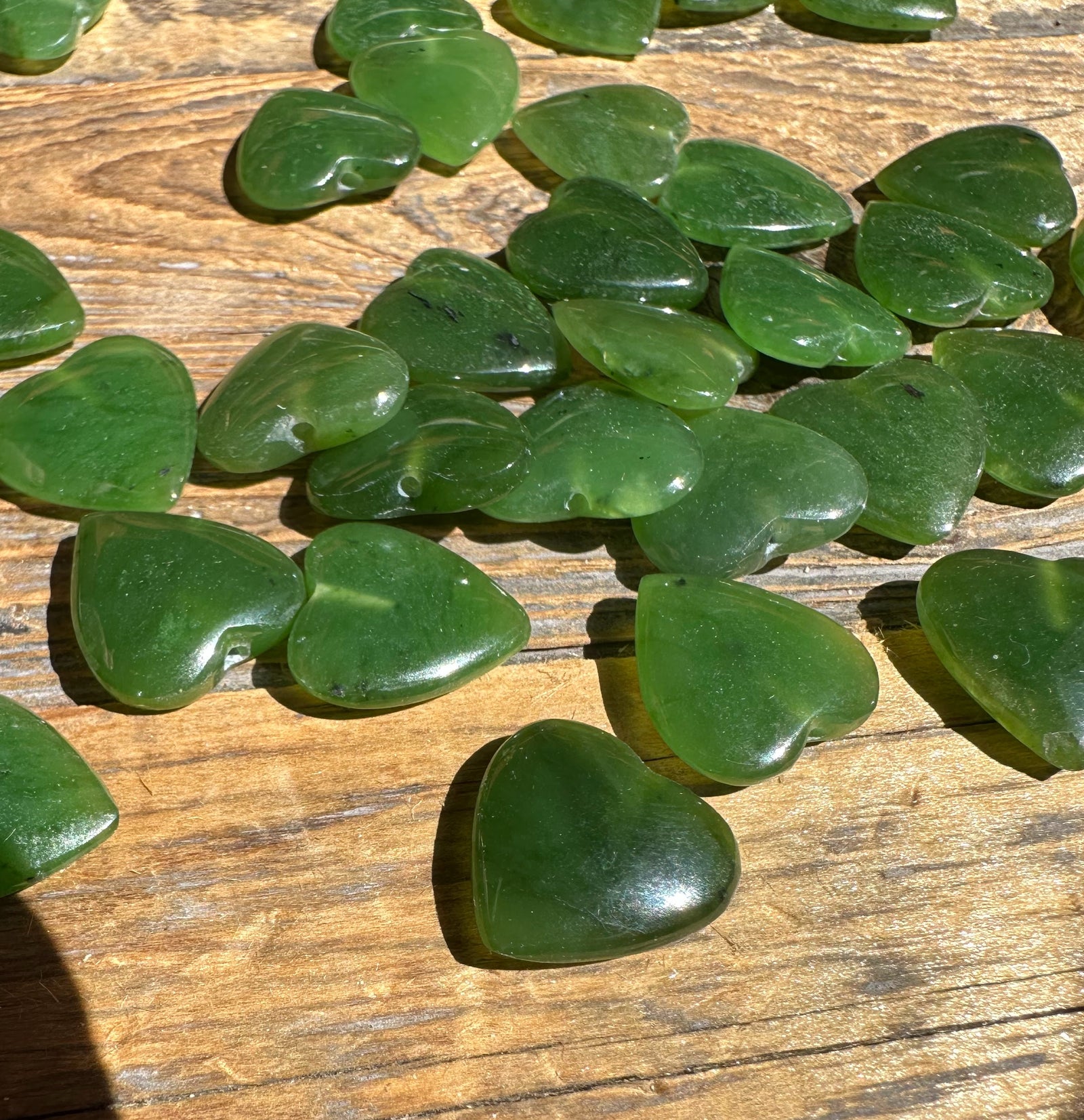 Close up of green jade heart beads with drilled holes spread on wood