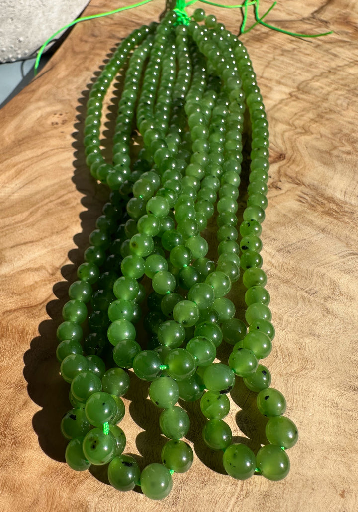 Group of glossy green 6mm beads ready for stringing on a bright green thread