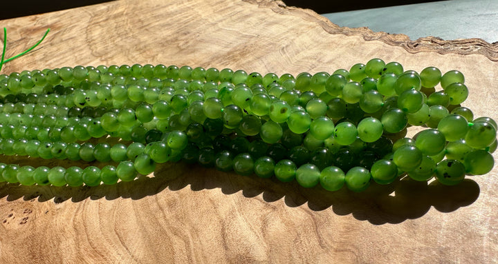 Green 6mm beads on several 16 inch unstrung strands laid on a wooden surface