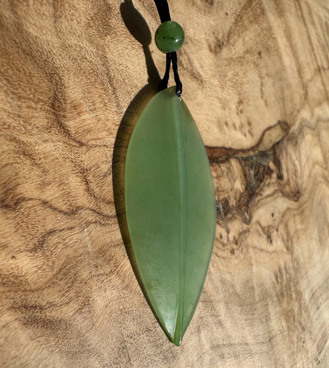 Siberian Jade Leaf Pendant 42mm on a black cord against textured wood surface