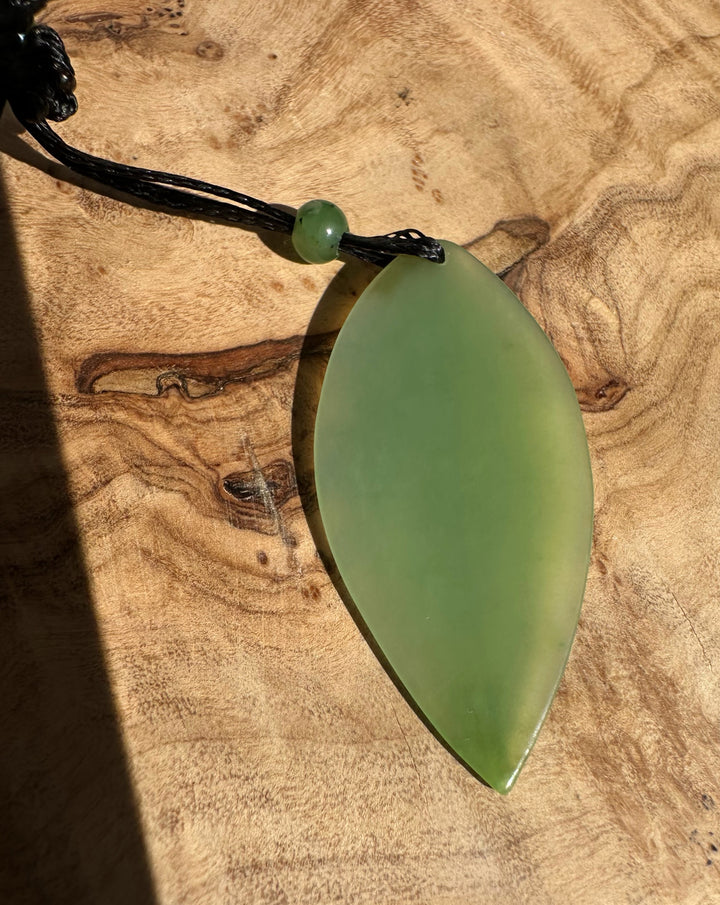 Close-up of Siberian Jade Leaf Pendant on black cord with a green accent bead against wood.
