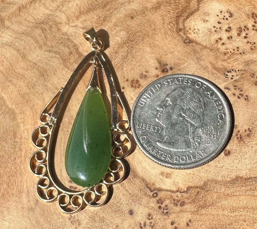 Close up of jade teardrop pendant with copper frame on wooden surface beside a quarter for scale