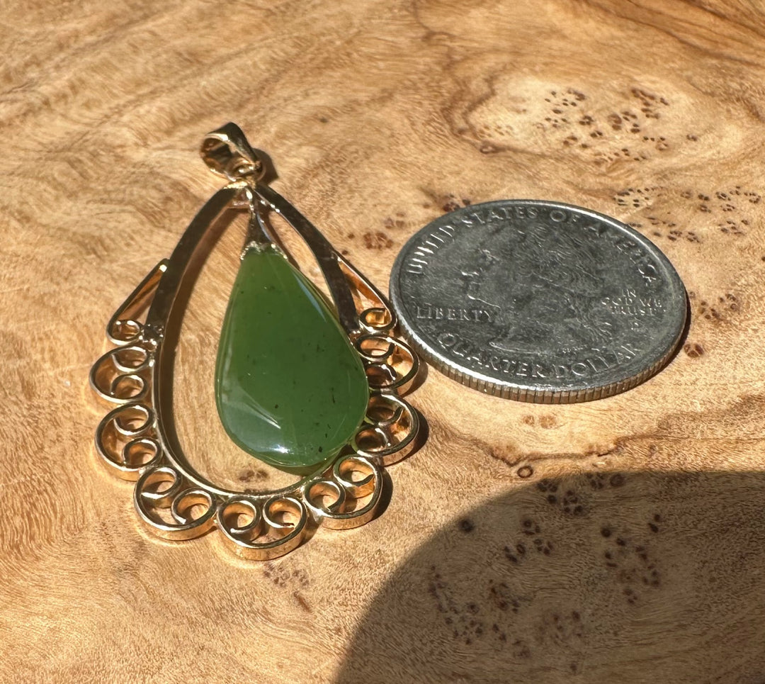 Nephrite jade teardrop pendant in copper frame placed on wood beside a quarter for scale