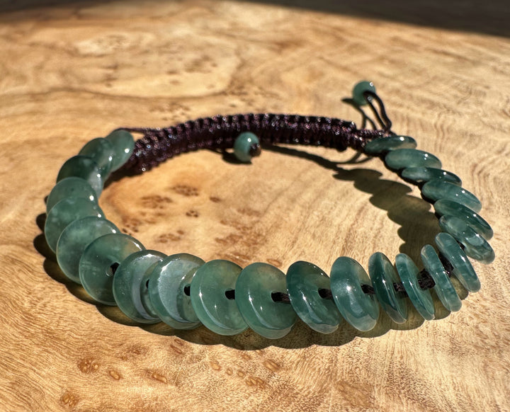 Guatemalan Jadeite PI Round Bracelet displayed on a wooden surface with a purple bead strand nearby.