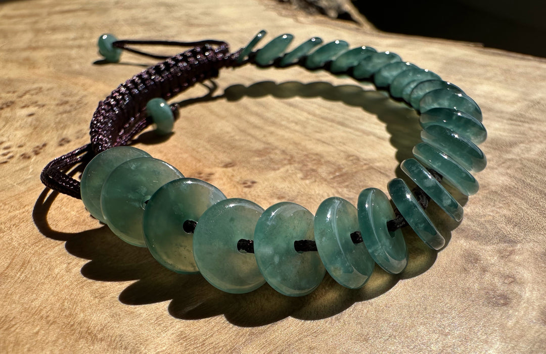 Guatemalan jadeite PI round bracelet with green flat discs on a dark braided cord on wood