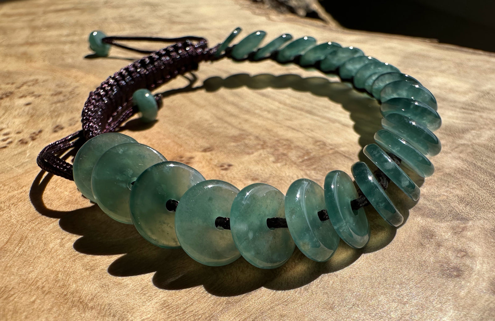 Guatemalan jadeite PI round bracelet with green flat discs on a dark braided cord on wood