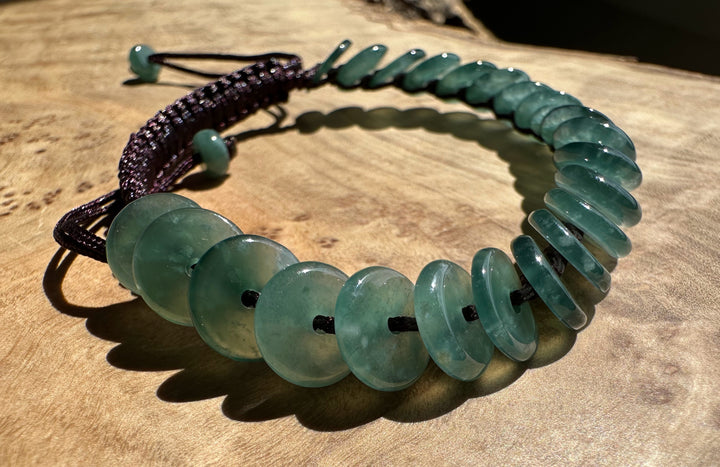 Guatemalan jadeite PI round bracelet with green flat discs on a dark braided cord on wood