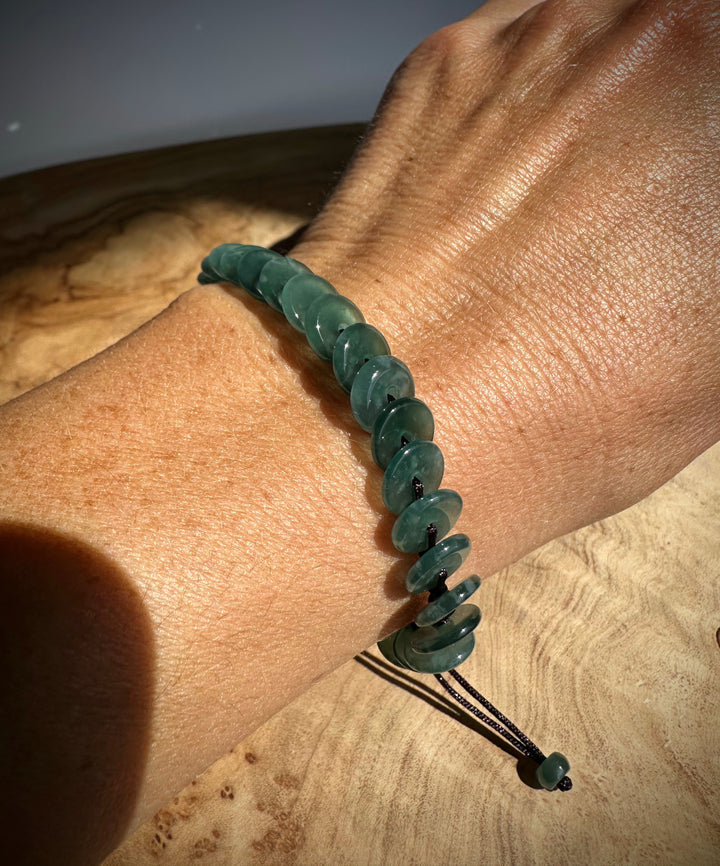 Guatemalan Jadeite PI Round Bracelet on the wrist beside a long purple bead strand.