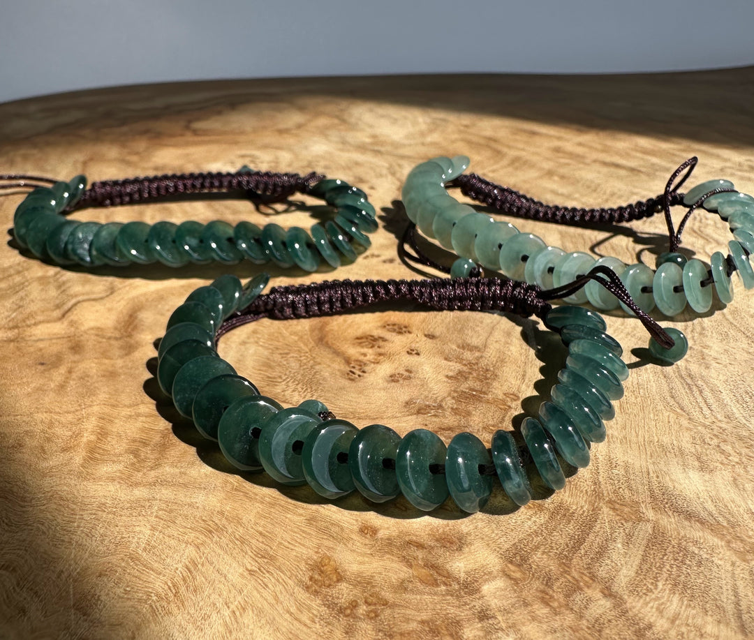 Guatemalan jadeite PI round bracelet with green discs coiled on a dark cord over a wooden surface