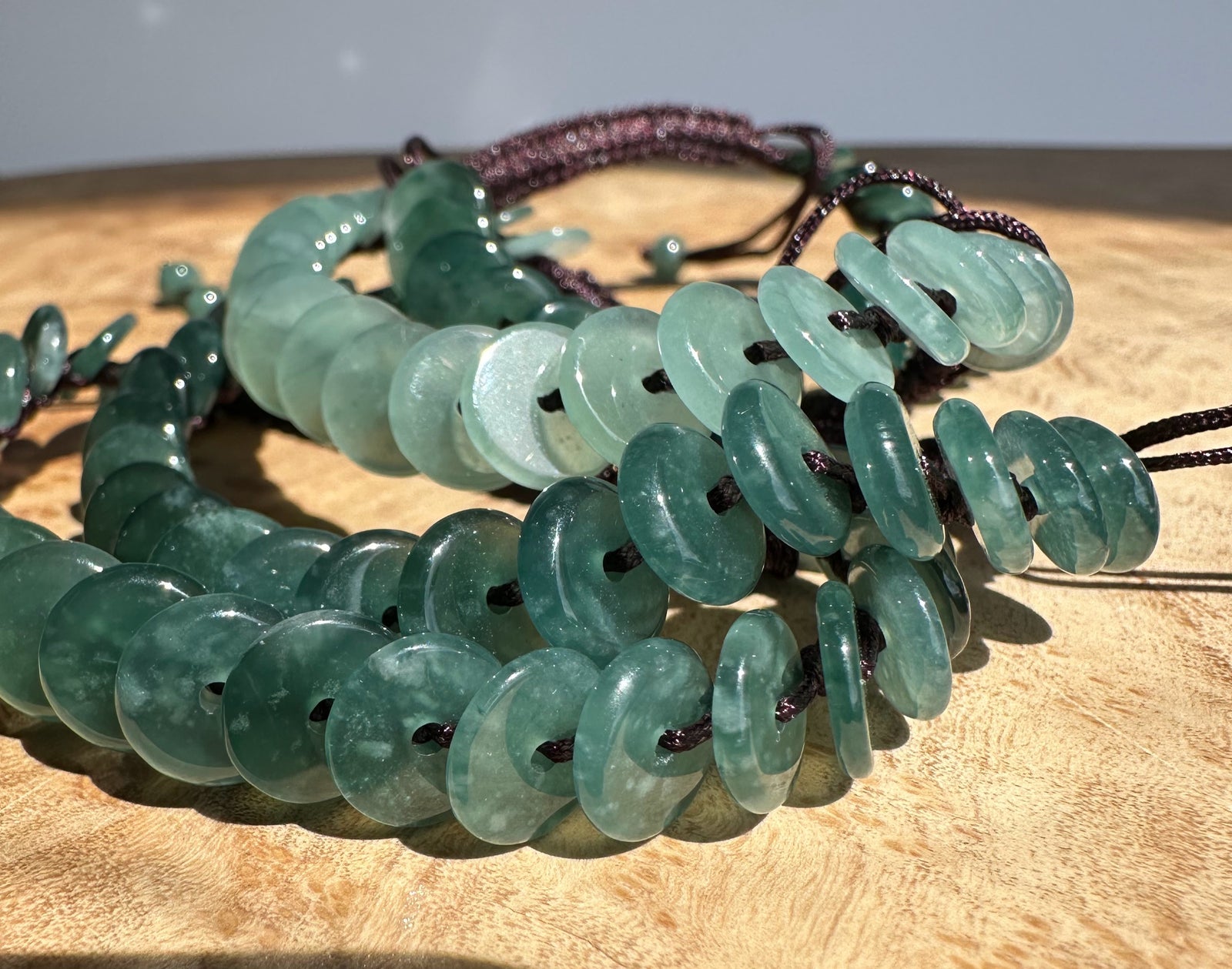 Guatemalan jadeite PI round bracelet with green discs on a dark purple braided cord on wood surface