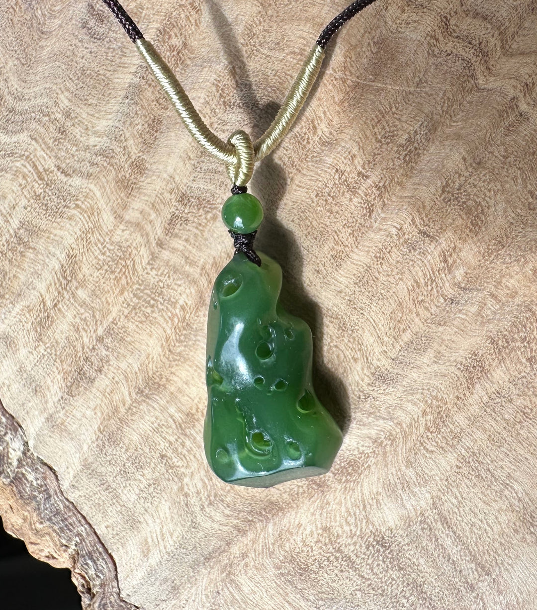 Rich green Siberian abstract pendant with a pale beige cord wrapped around the top, displayed on textured fabric.