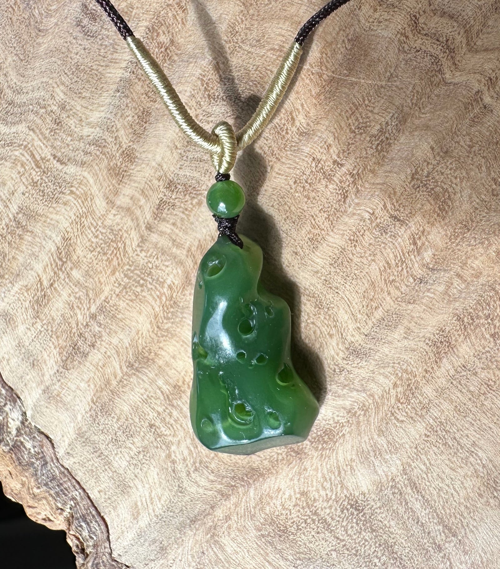 Rich green Siberian abstract pendant with a pale beige cord wrapped around the top, displayed on textured fabric.