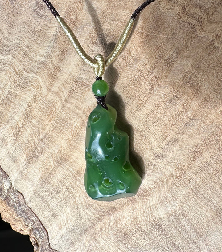 Rich green Siberian abstract pendant with a pale beige cord wrapped around the top, displayed on textured fabric.