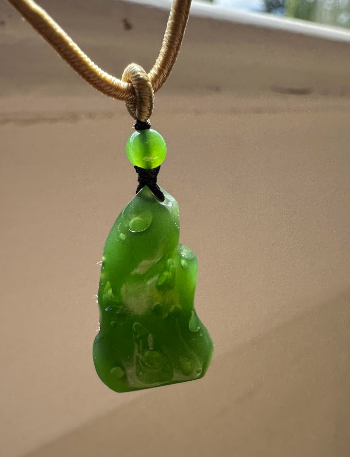 Close-up of lime green bead above the green abstract pendant on a tan braided cord
