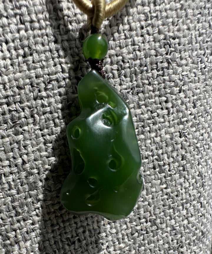 Glossy green jade pendant with circular holes against a gray woven fabric background