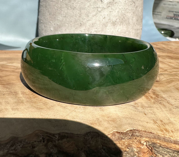 Side view of the green Canadian nephrite jade oval bangle with a glossy finish on wood