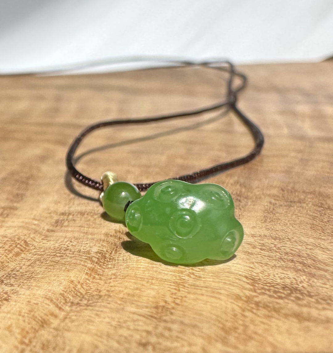 Close up of brown braided cord with a small green jade bead and knot near the pendant