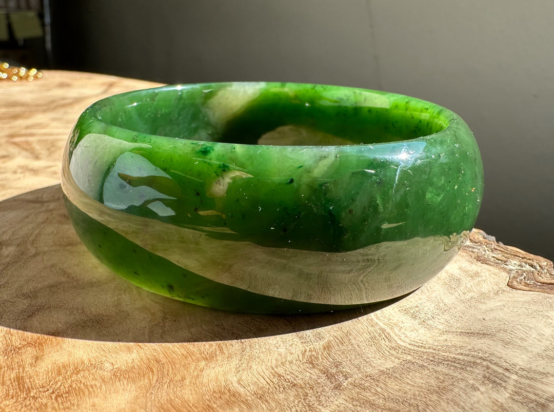 Jade Oval Bangle 68mm Canadian nephrite jade with green and light banding resting on a wood surface