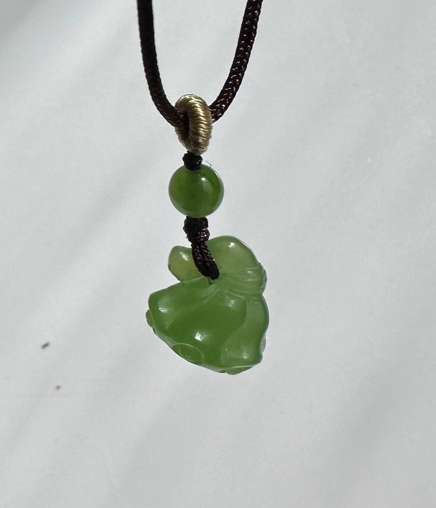 Green jade bead above a carved jade pendant on a brown cord with a wrapped loop