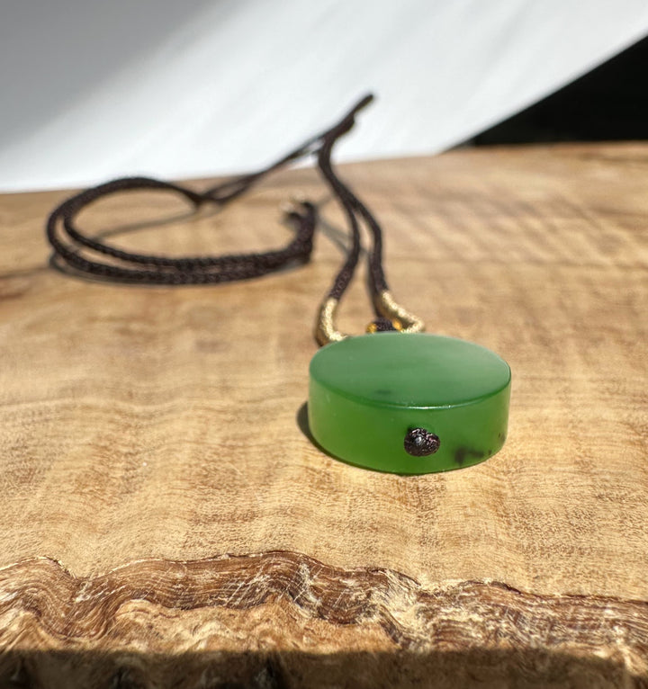 Apple green Siberian jade pendant on a brown braided cord resting on a wooden surface.