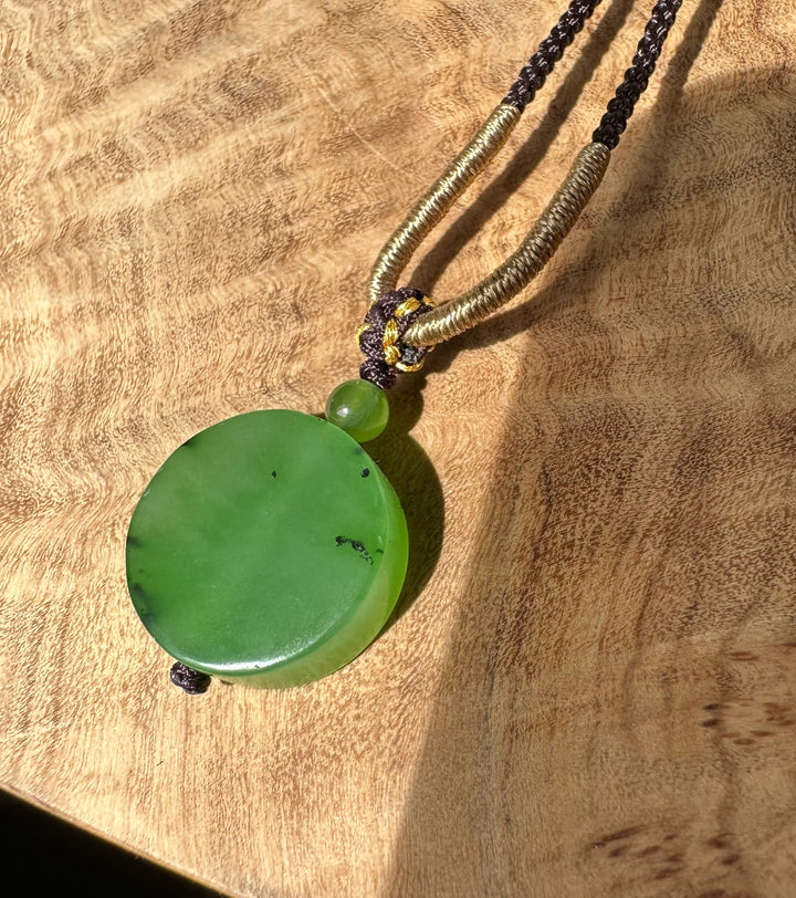 Large round apple green jade pendant attached to braided cords with a decorative knot on a brown textured background