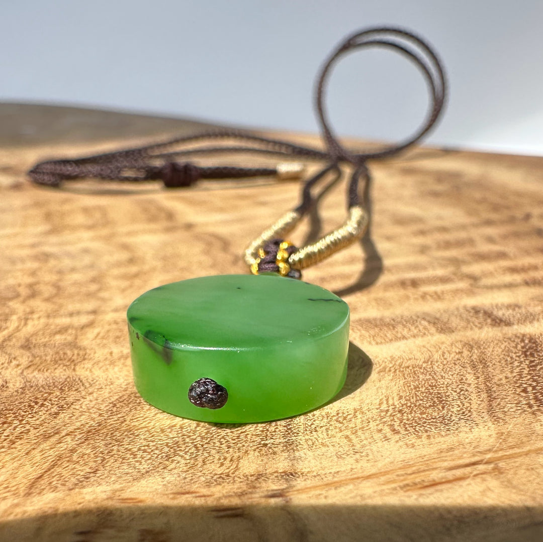 Apple green jade pendant with brown braided cord and decorative knot resting on a wooden surface