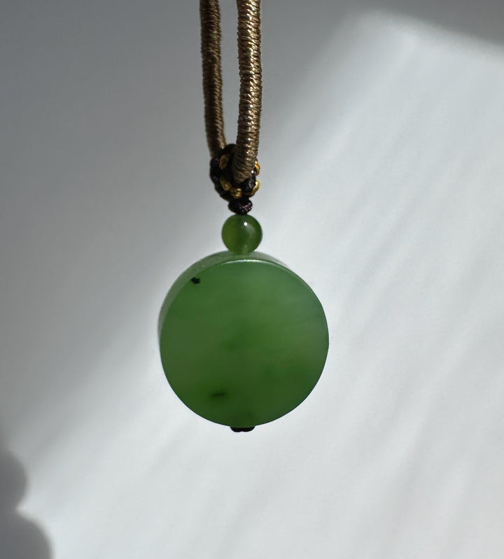 Apple green jade pendant on a gold braided cord with a knotted centerpiece and bead accents