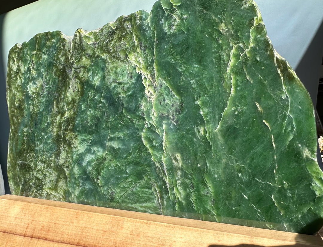Canadian jade slab on a light wooden base with rough jagged edges and deep green color.