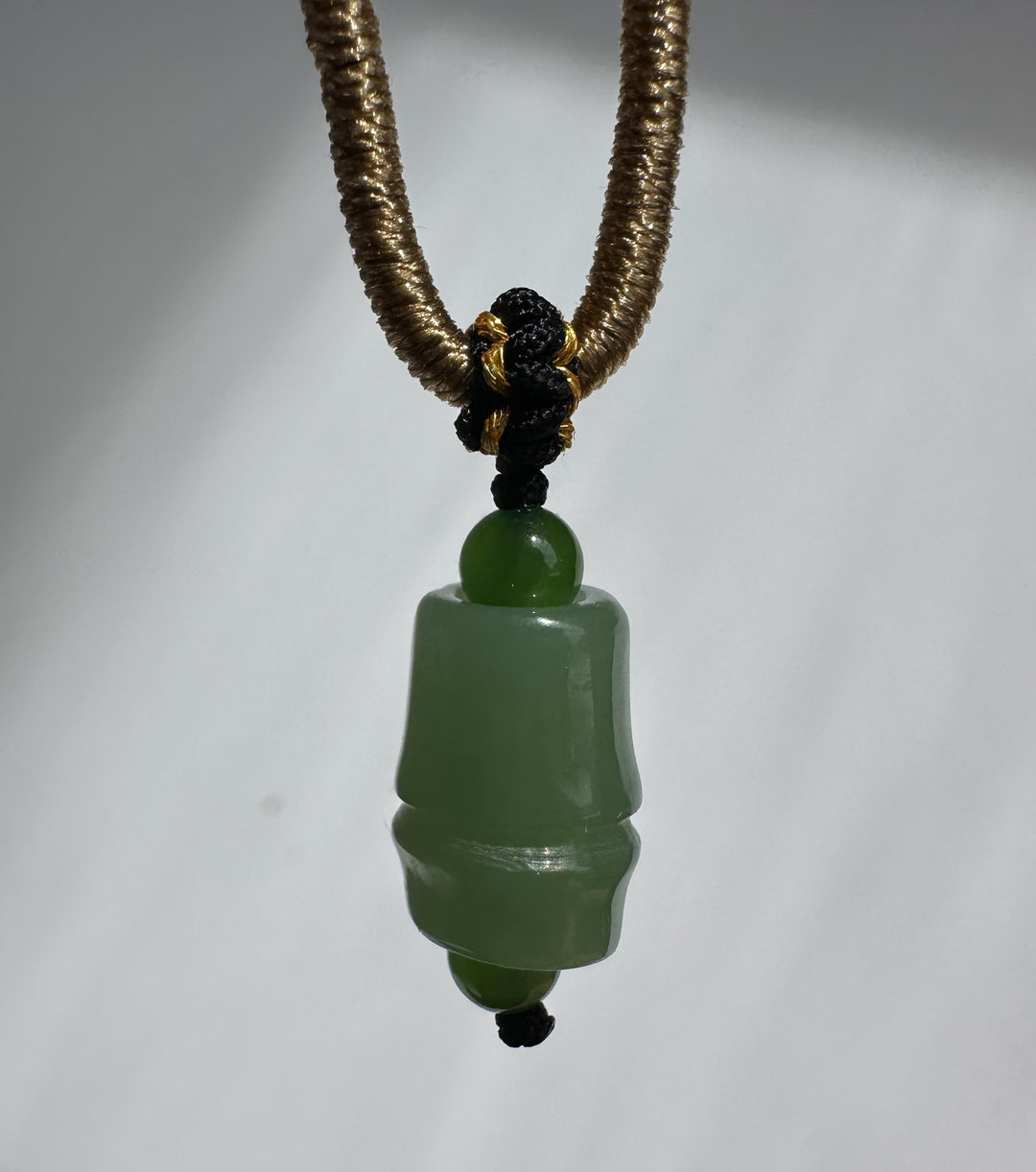 Close up of Siberian Jade Pendant showing gold coil wrapping and black cord with jade bead and a coin for scale
