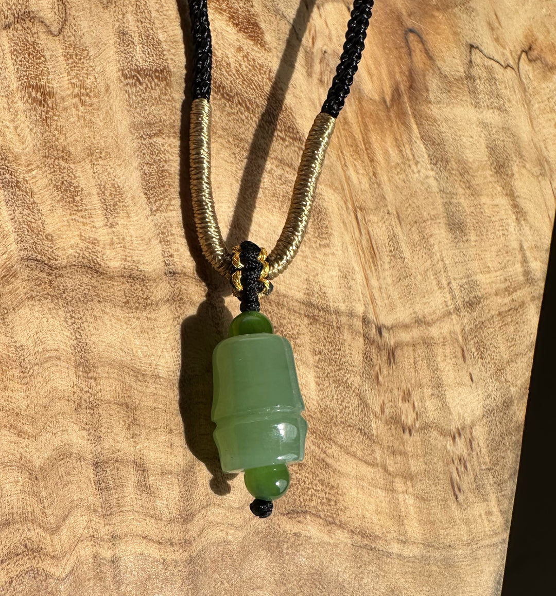 Siberian jade pendant on a black braided cord with gold coil accents against a wooden background