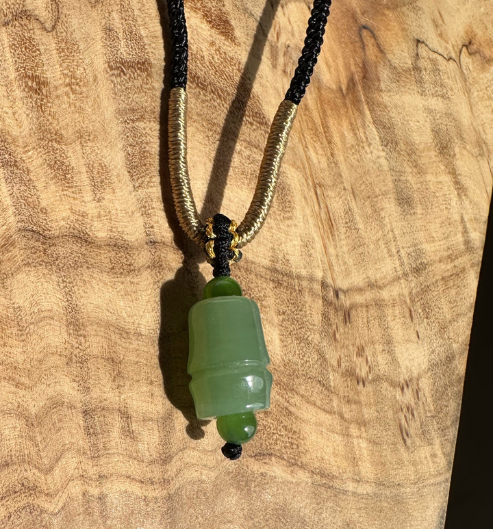 Siberian jade pendant on a black braided cord with gold coil accents against a wooden background
