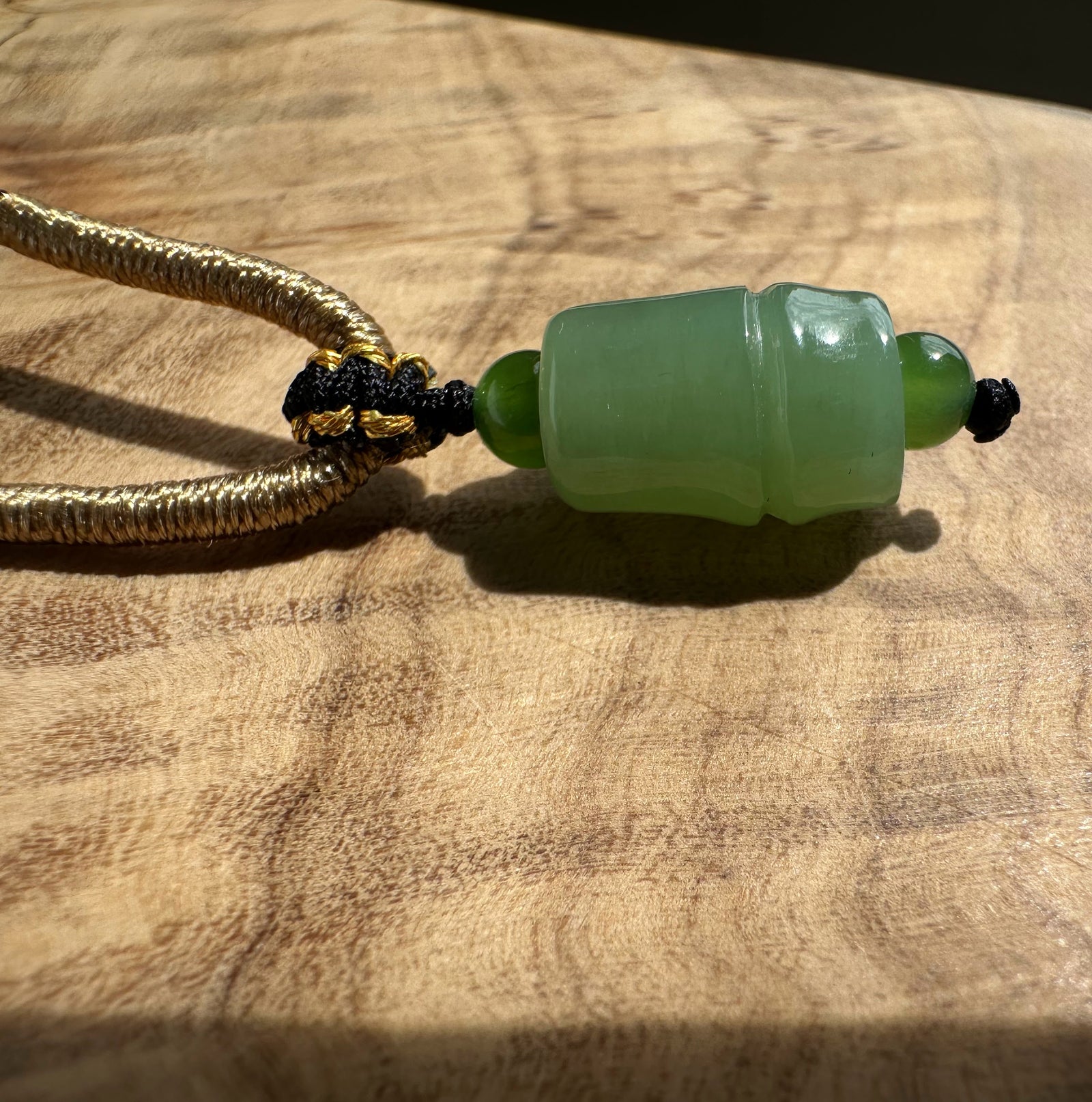 Siberian jade pendant on a textured brown braided cord with gold accent knots.