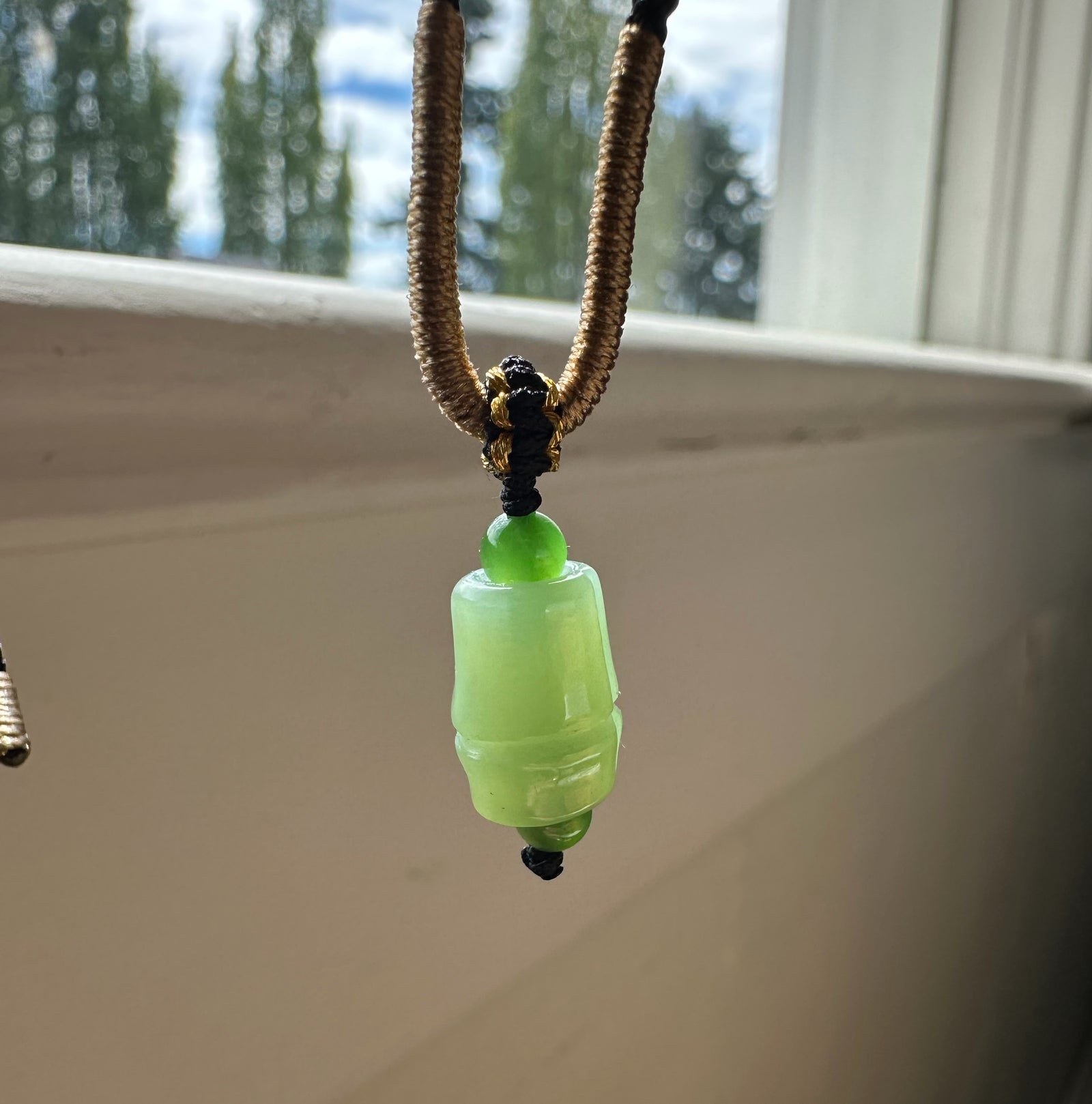 Close up of a green jade bead and cylindrical pendant threaded on a brown cord.