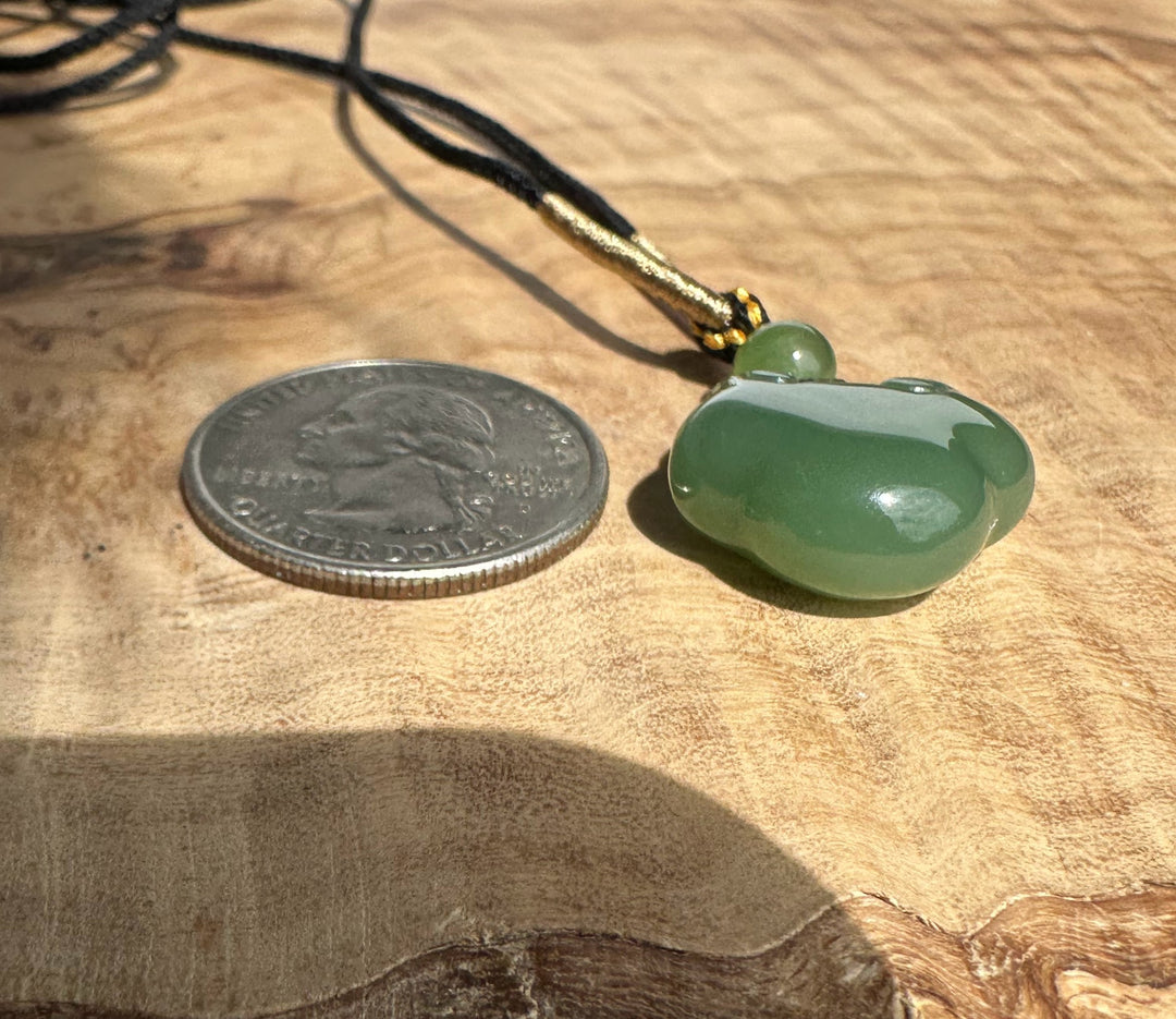 Green nephrite jade Ruyi pendant on a black and gold cord with a coin for scale