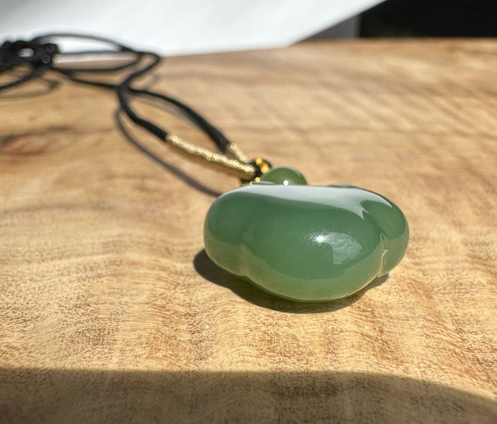 Close up of black cord with gold wrap and a small green jade bead beside the pendant