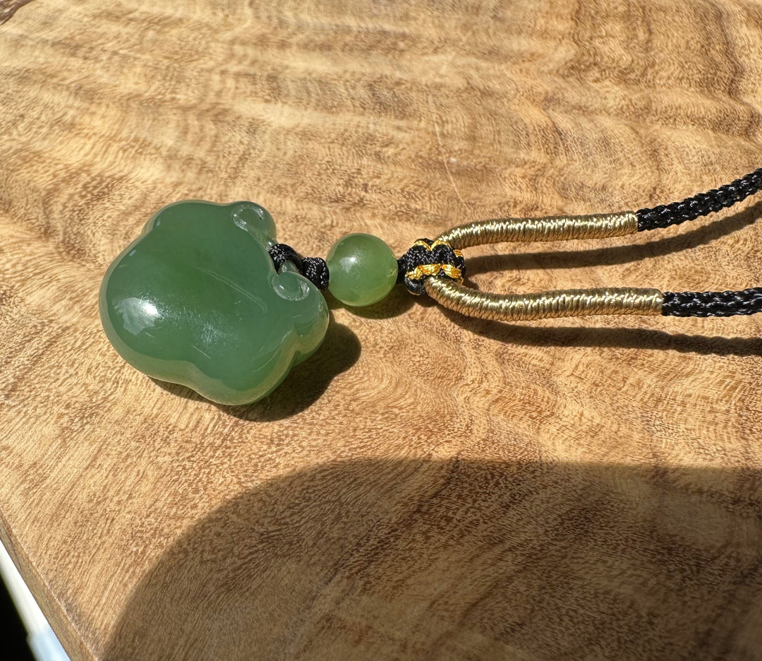 Large green nephrite jade Ruyi pendant on black and gold cord against a textured tan surface