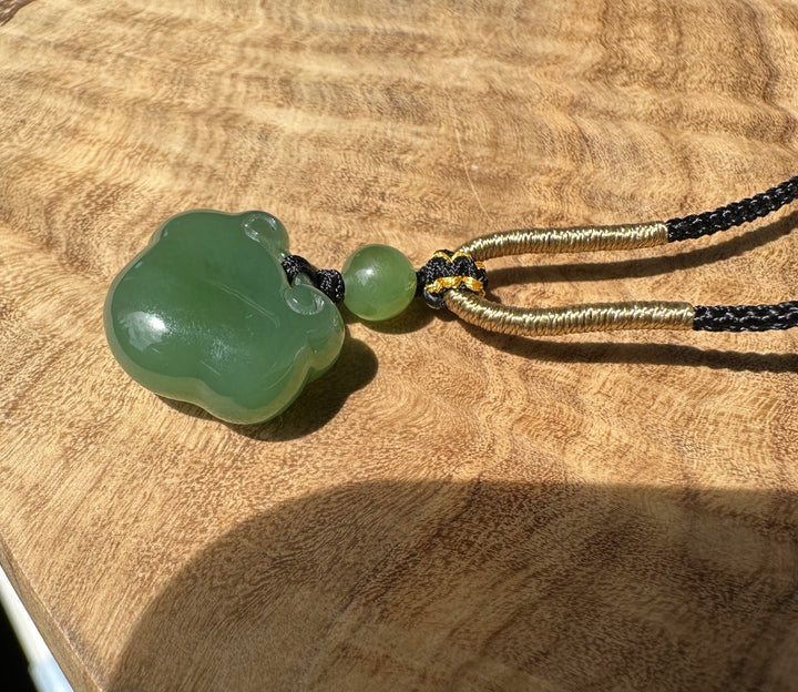 Large green nephrite jade Ruyi pendant on black and gold cord against a textured tan surface