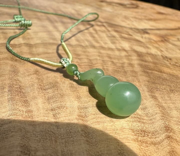 Close-up of Siberian nephrite Hulu pendant components a round bead and curling drop on a green cord