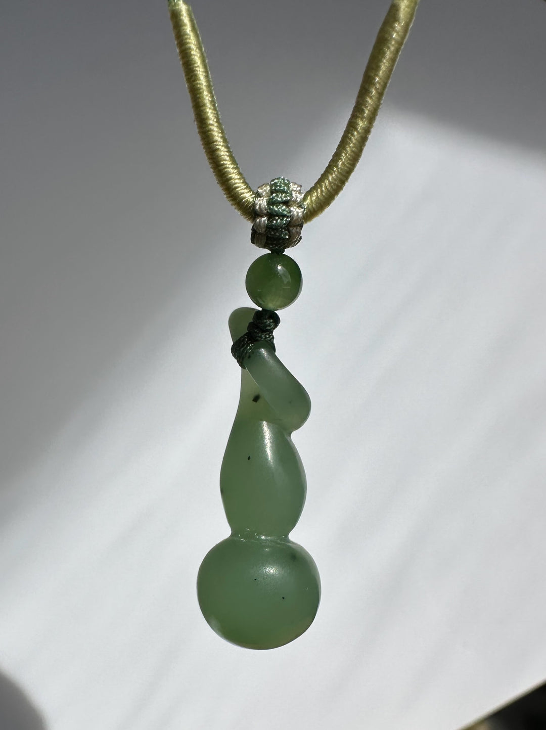 Hulu pendant with knotted green nephrite beads and gold cord against a white studio background