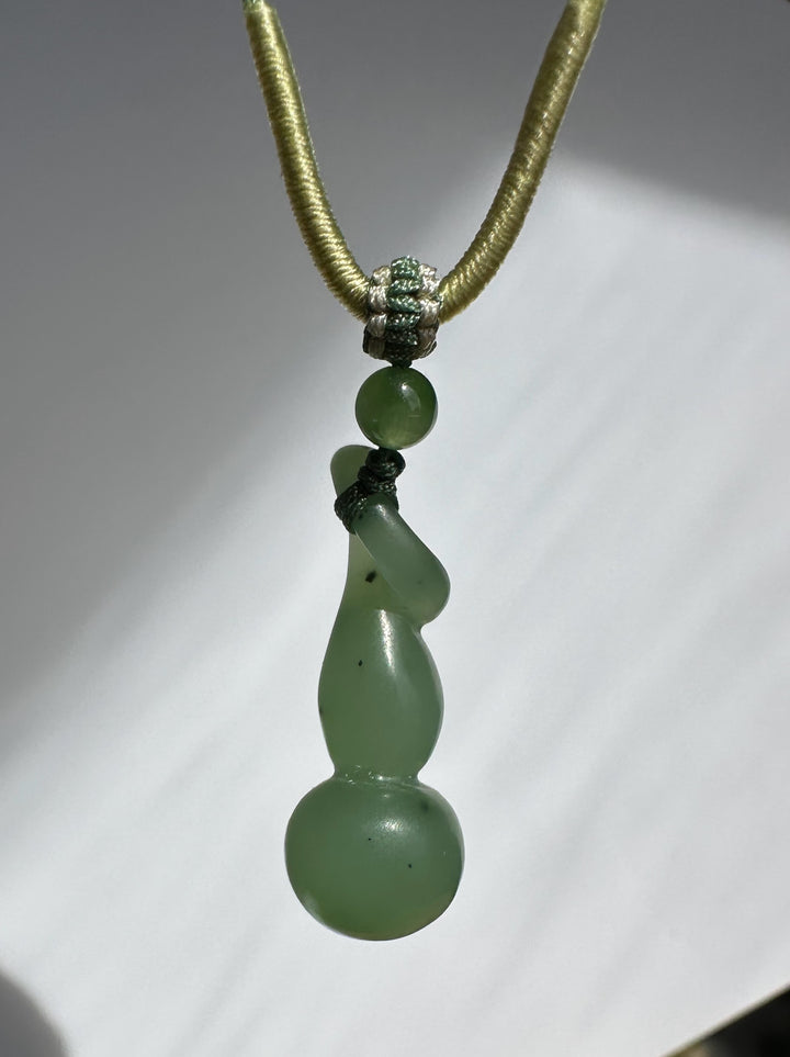 Hulu pendant with knotted green nephrite beads and gold cord against a white studio background