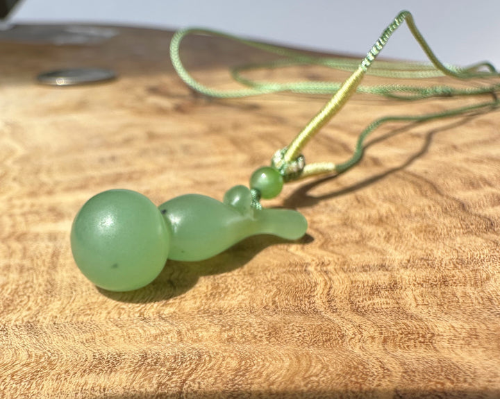 Siberian nephrite Hulu pendant with green beads on a pale green cord resting on a wood surface