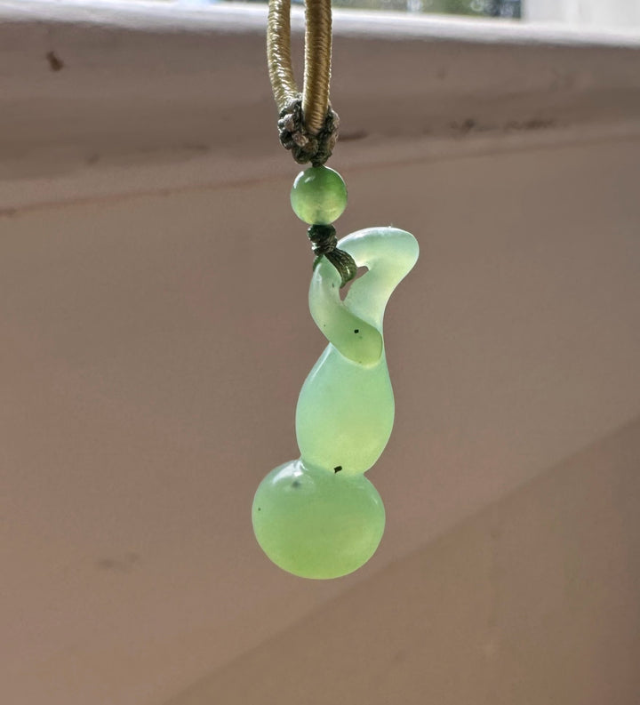 Close-up of the Hulu pendant top with a knotted cord and a round nephrite bead on a wood background