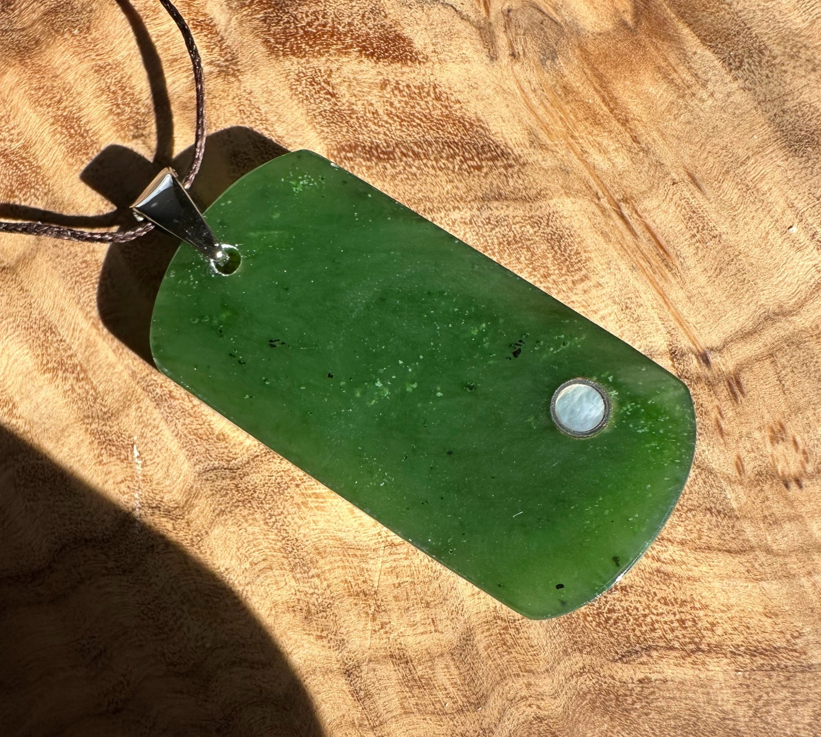 Green jade dog tag pendant with a metal accent on a brown cord