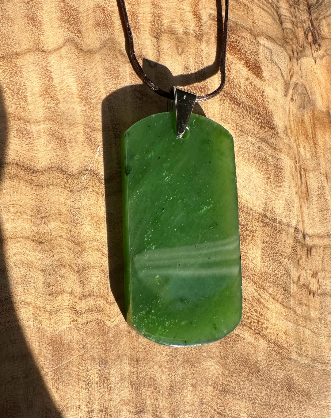 Dark green jade dog tag pendant on a brown cord laid on a wooden surface