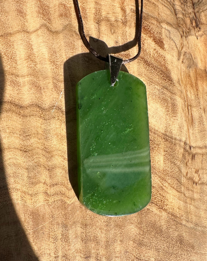Dark green jade dog tag pendant on a brown cord laid on a wooden surface