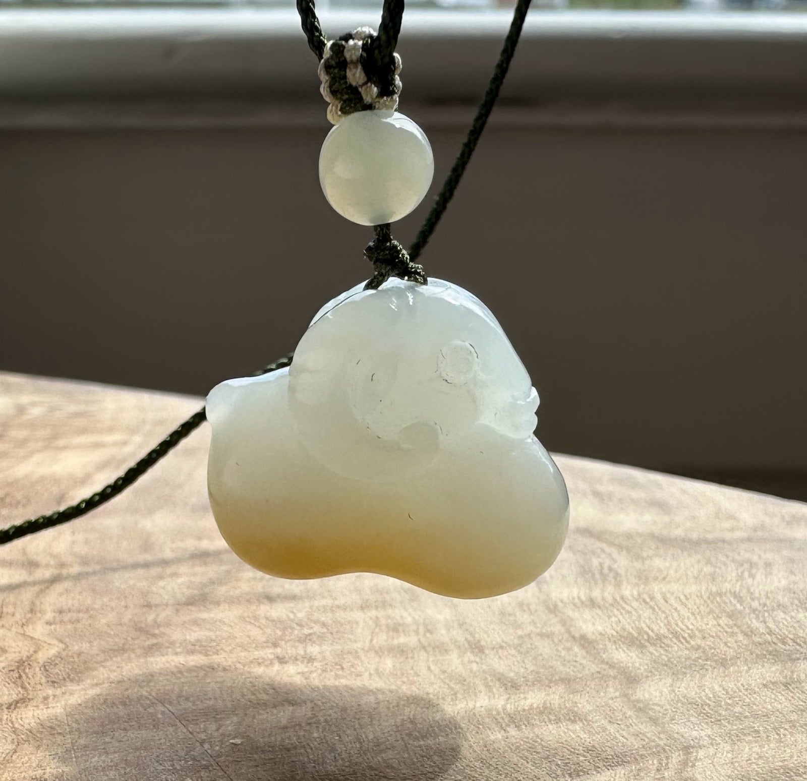 White and brown jade pendant hanging with a blurred background