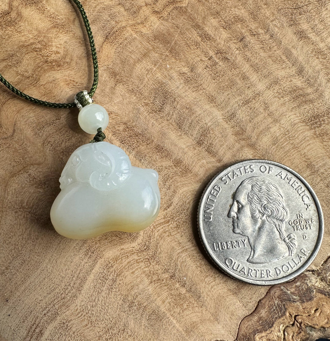 White and brown jade pendant on a wood surface beside a quarter for scale